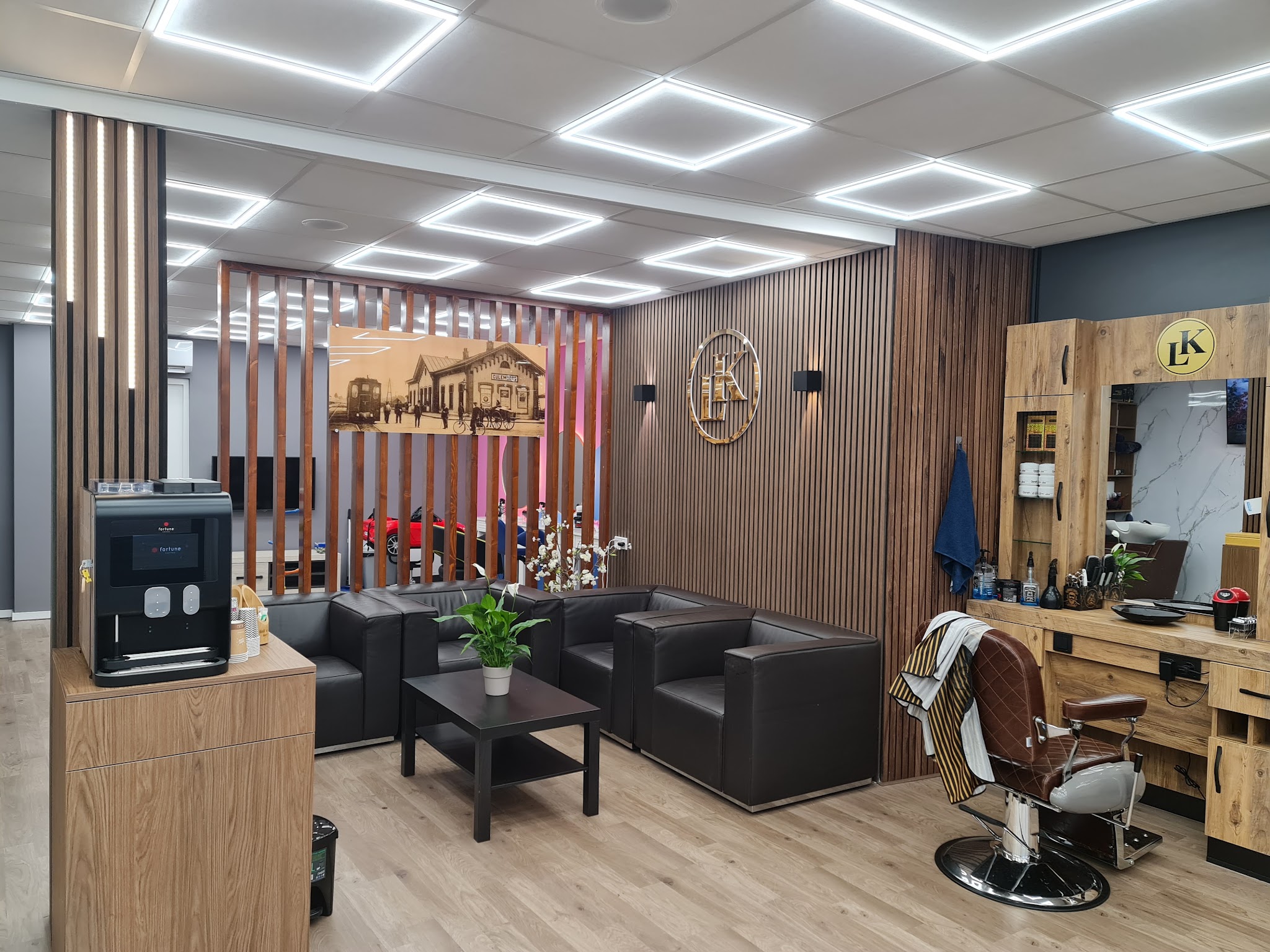 De zithoek met zwarte banken, een koffiemachine en de eiken lamellenwand met het LK-embleem
