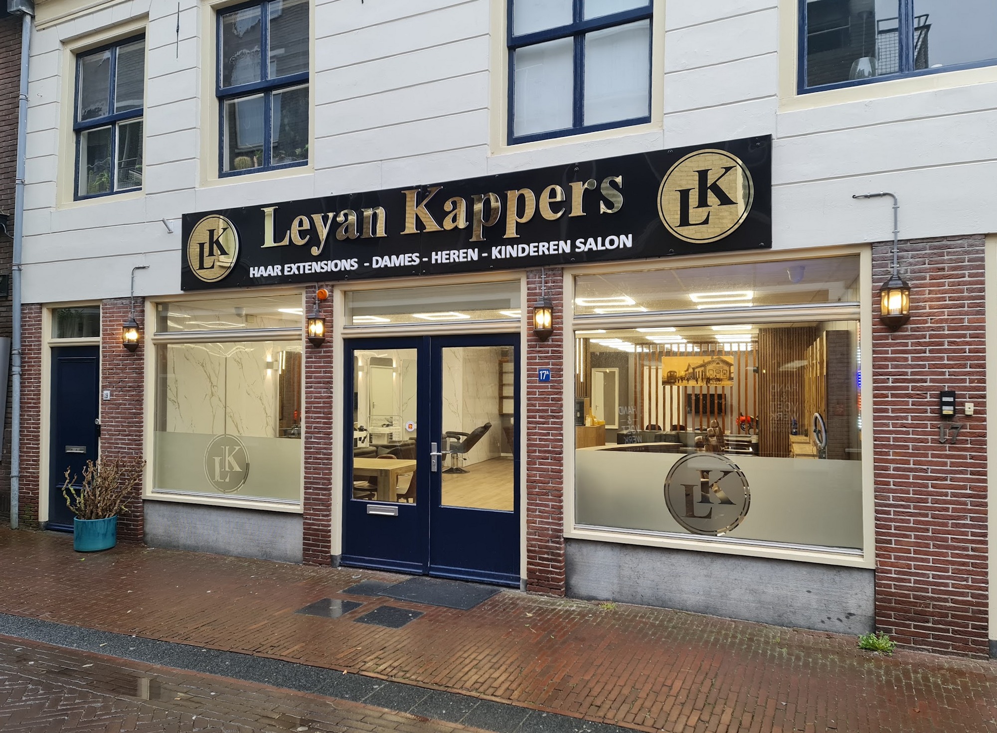 De gevel van Leyan Kappers aan de Everwijnstraat: een zwart uithangbord met gouden letters en twee LK-emblemen boven drie ramen en een blauwe dubbele deur