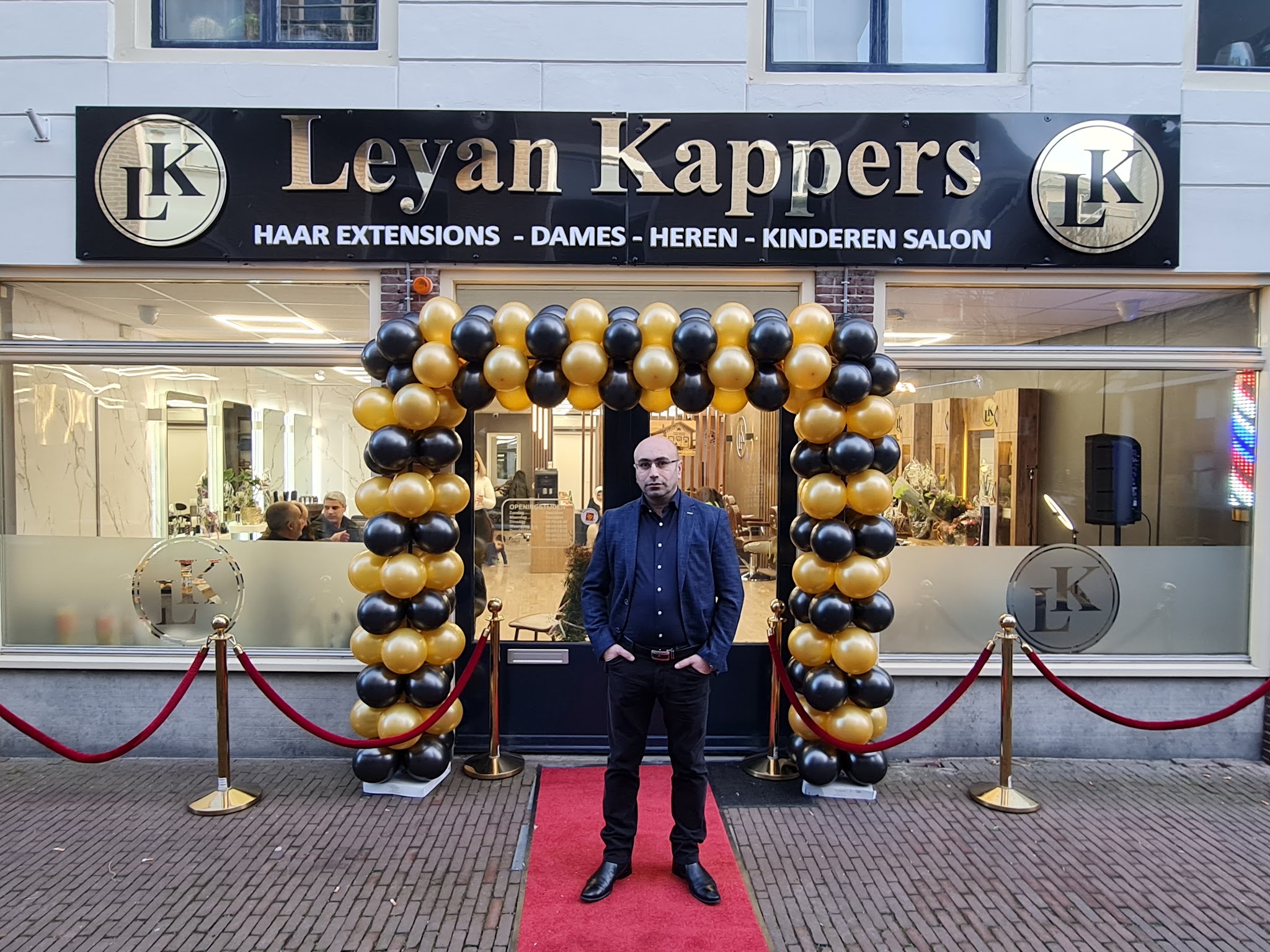 De gevel van Leyan Kappers met een zwart-gouden ballonnenboog, een rode loper en het uithangbord met de twee LK-emblemen