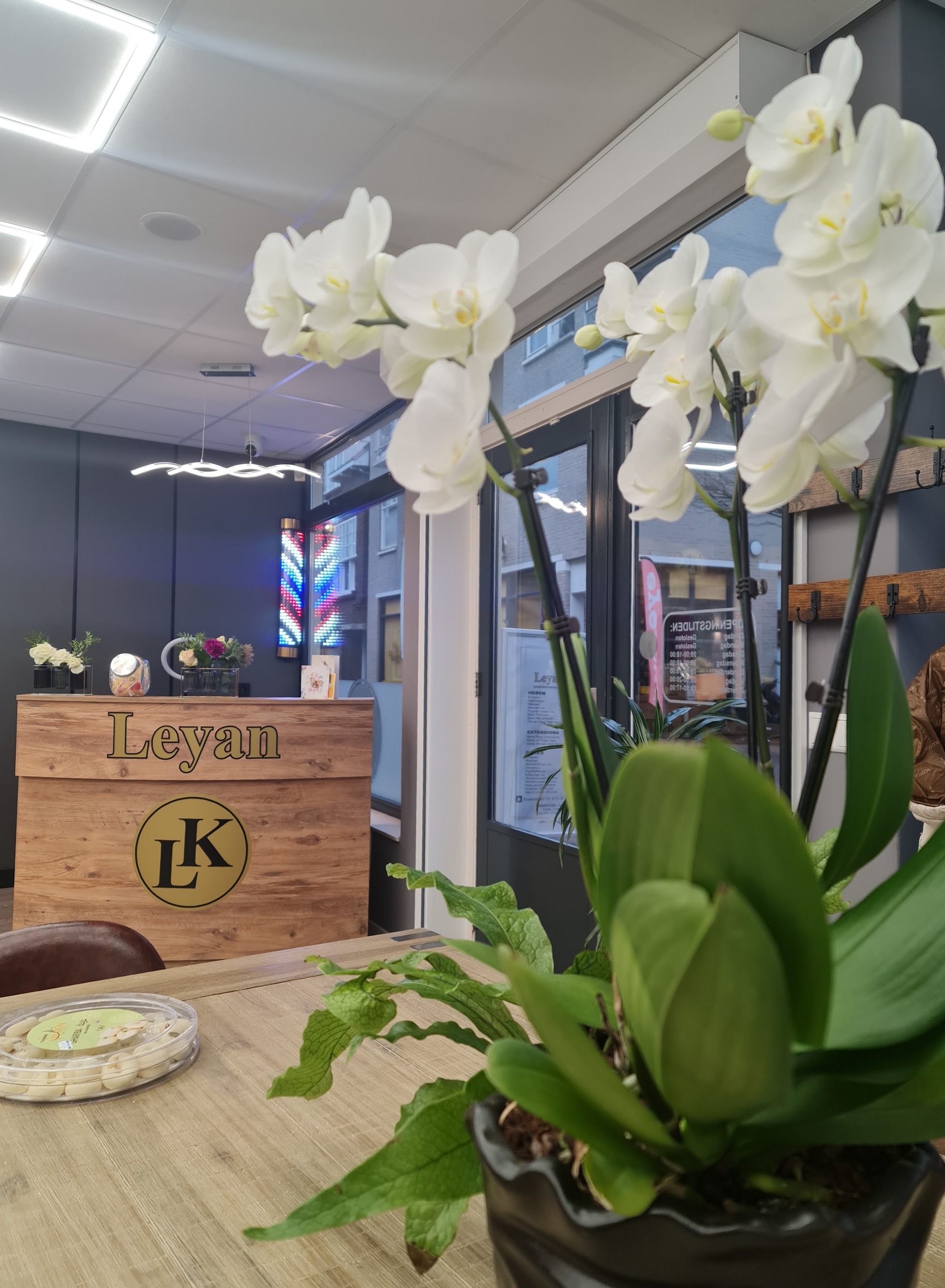 De eiken balie met de naam Leyan en het LK-embleem, witte orchideeën op tafel en een kapperspaal bij het raam