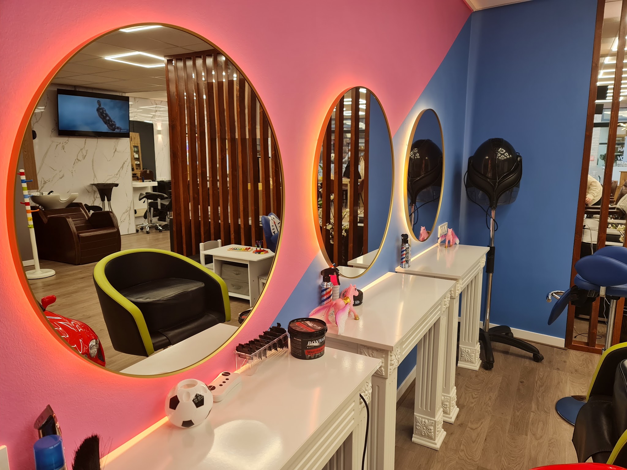 De kinderhoek met ronde verlichte spiegels, een kleine kappersstoel en een roze en blauwe wand